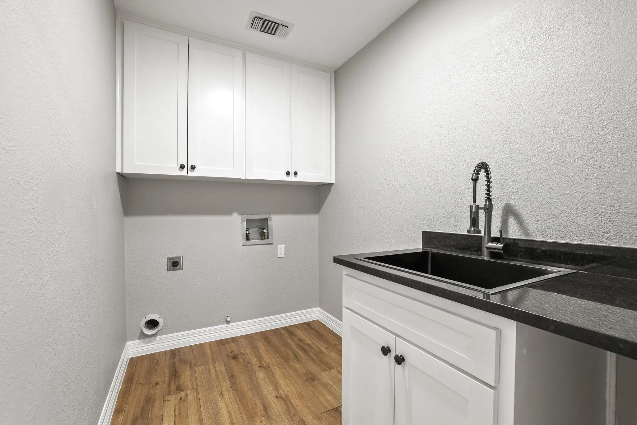 Laundry area featuring wood-finish flooring, white cabinetry, a dark utility sink, and dark countertops