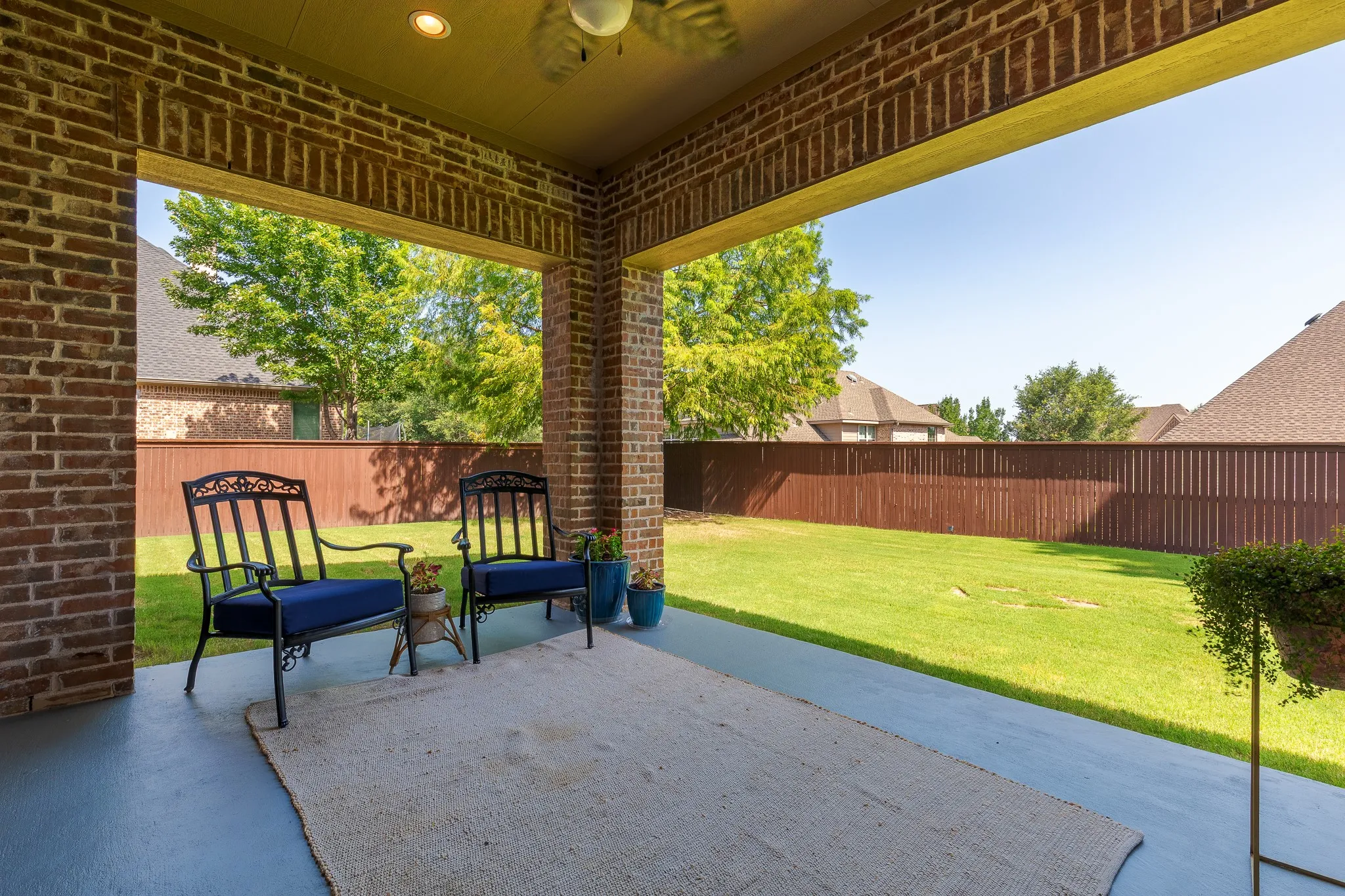Covered patio with brick columns and ceiling fan overlooking the backyard.