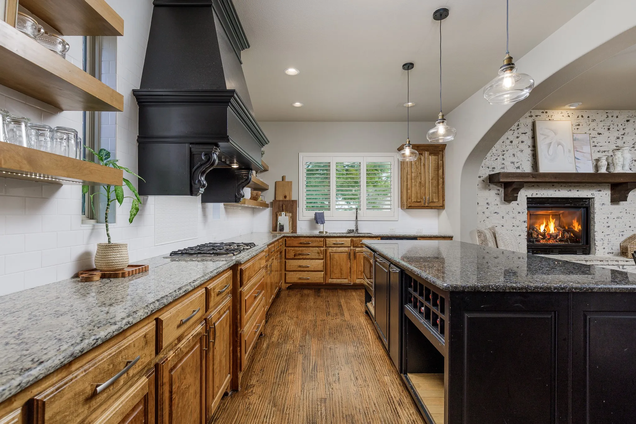 Gourmet kitchen featuring a built-in gas range, large black range hood, light wood-finish cabinetry, and an abundance of light.