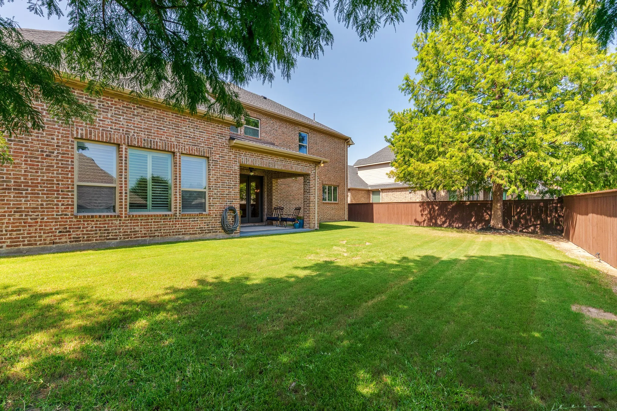 Spacious backyard featuring a manicured lawn, a full brick exterior, a covered patio, and a privacy fence