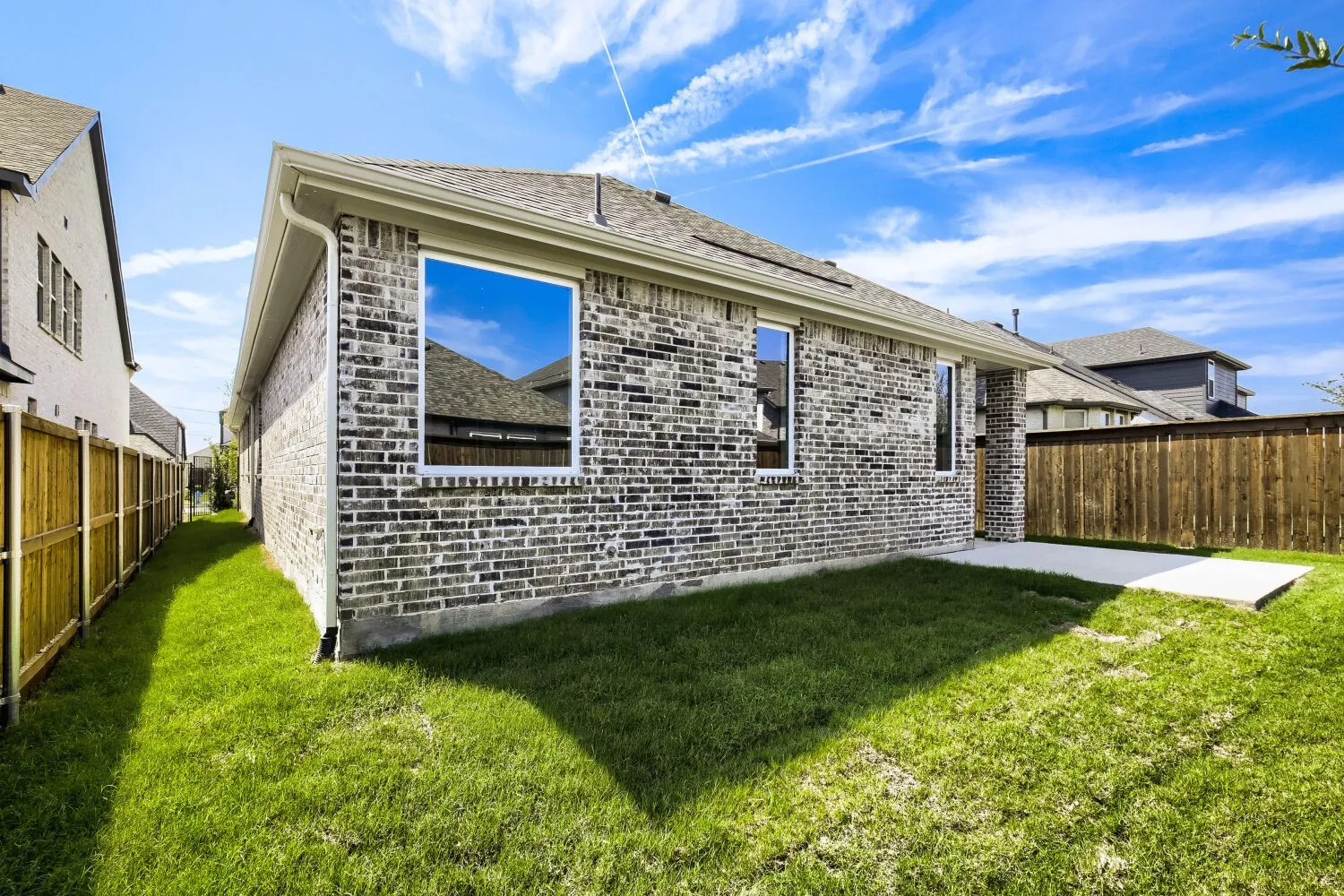Brick exterior construction with white window frames, a concrete patio, and a wood privacy fence