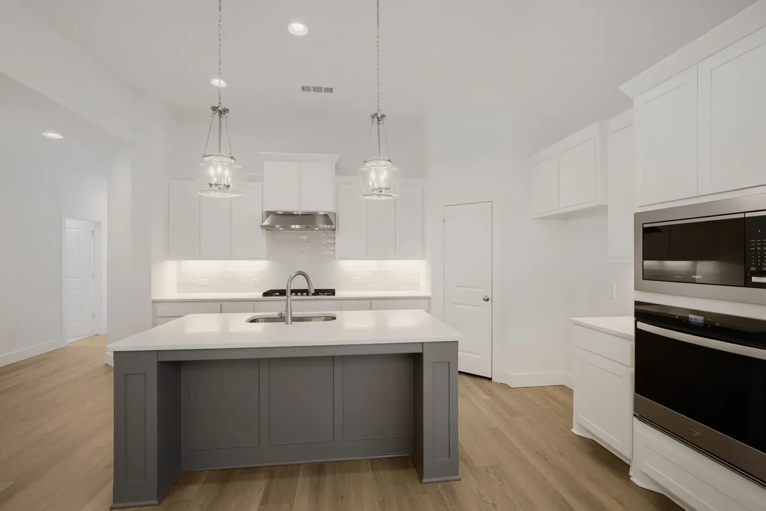 Kitchen featuring a gray island with a white countertop, stainless steel appliances, white cabinetry, and wood-finish flooring