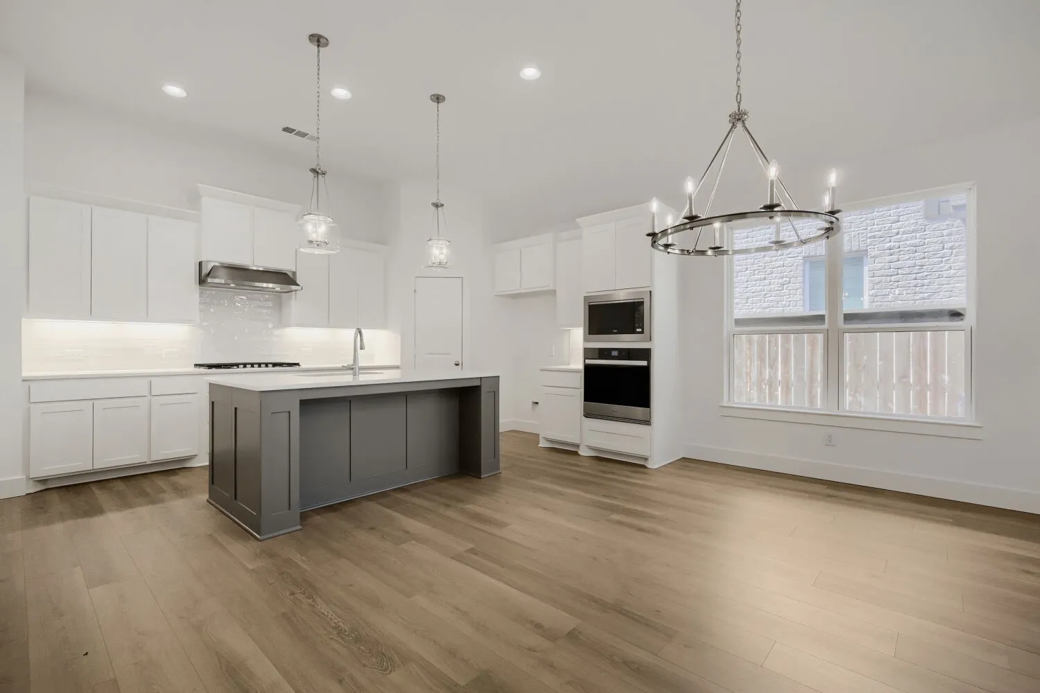 Open-concept kitchen featuring a spacious island, stainless steel appliances, white cabinetry, and wood-finish flooring