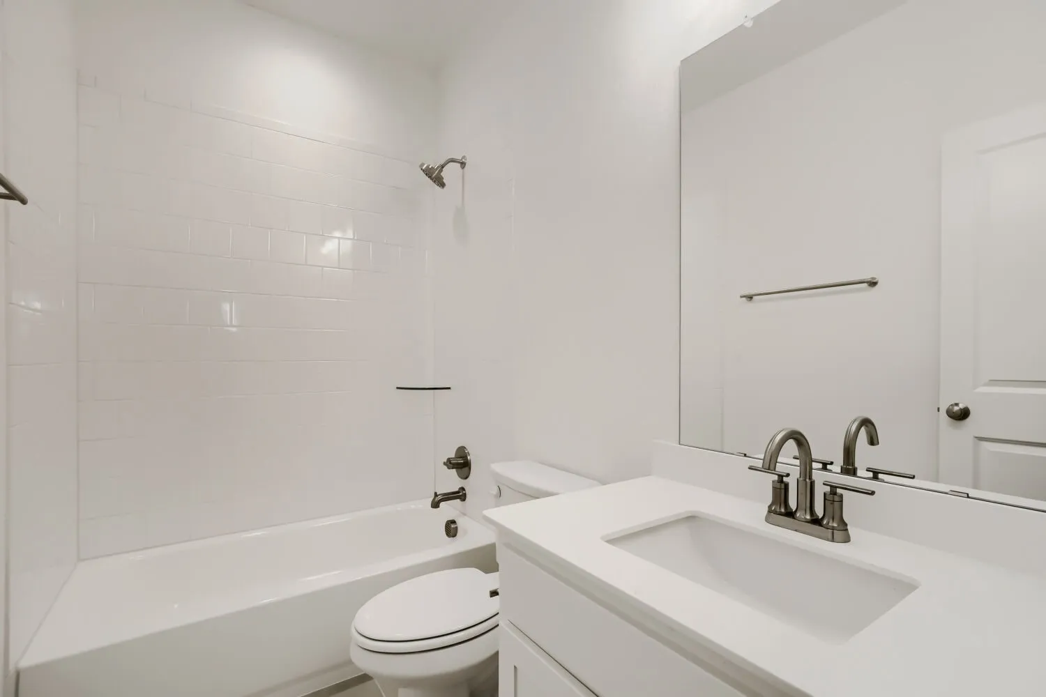 White subway tile tub surround, white vanity with integrated sink, brushed nickel faucet, large wall-mounted mirror
