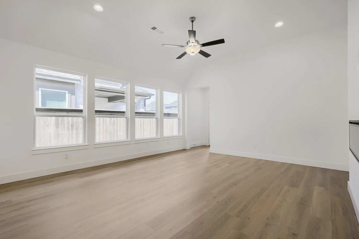 Spacious room featuring wood-finish flooring, vaulted ceiling, recessed lighting, a modern ceiling fan, and a wall of windows
