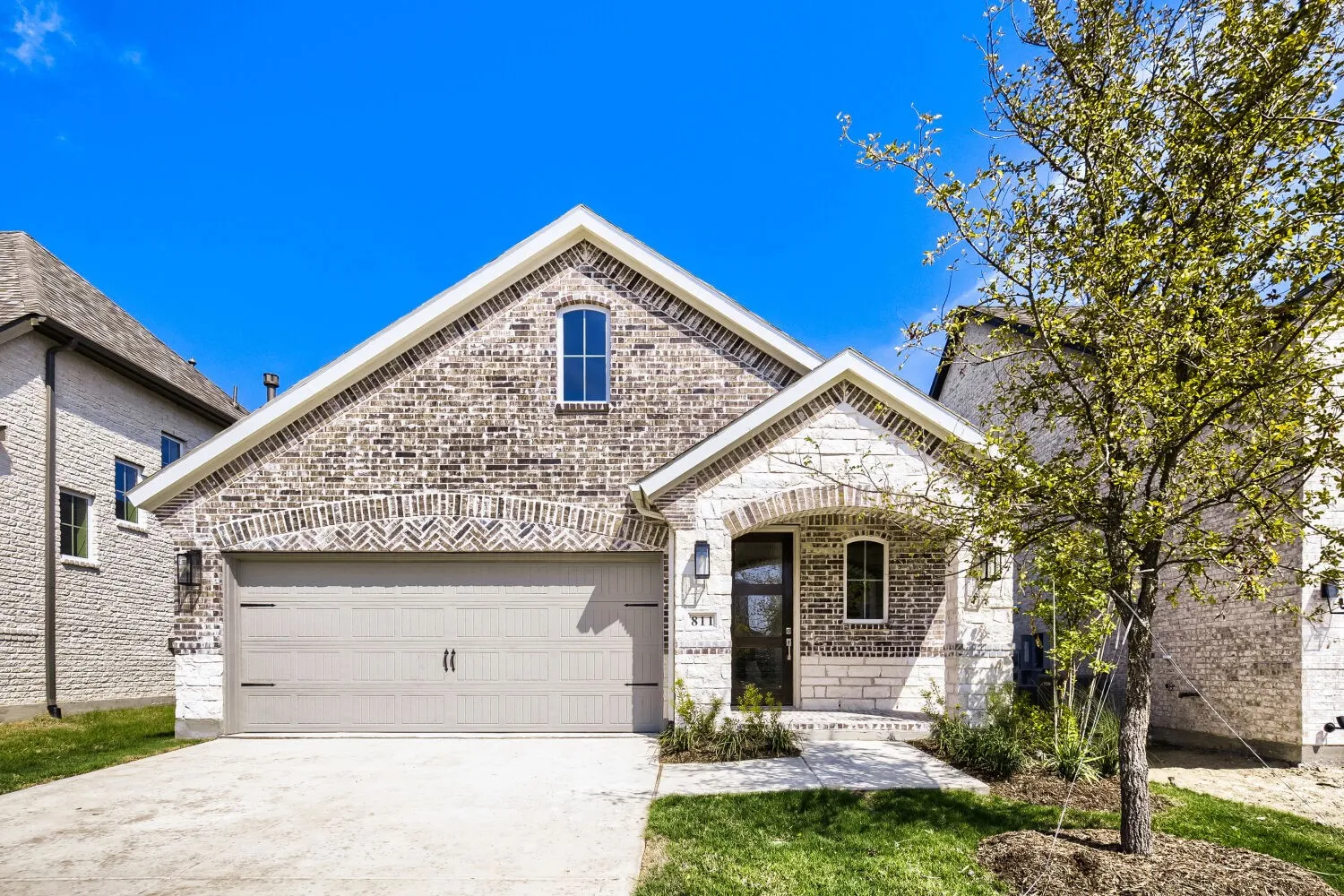 Brick and stone exterior with an arched entryway, attached two-car garage, and concrete driveway