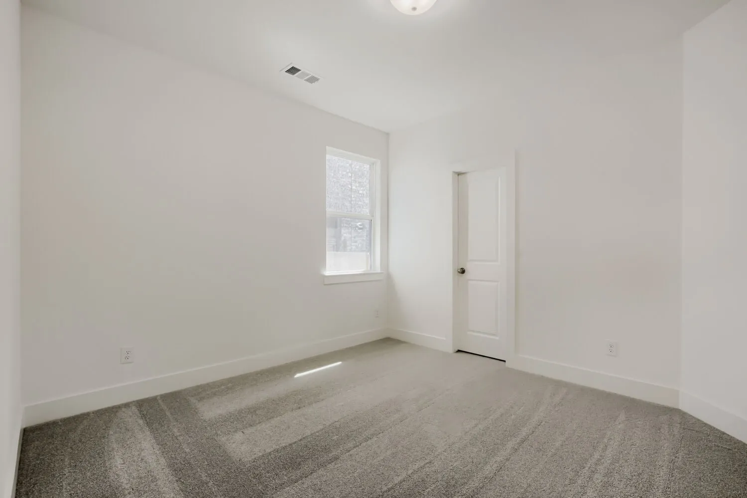 Recessed ceiling light, neutral wall color, patterned gray carpet, white trim, and a paneled white door