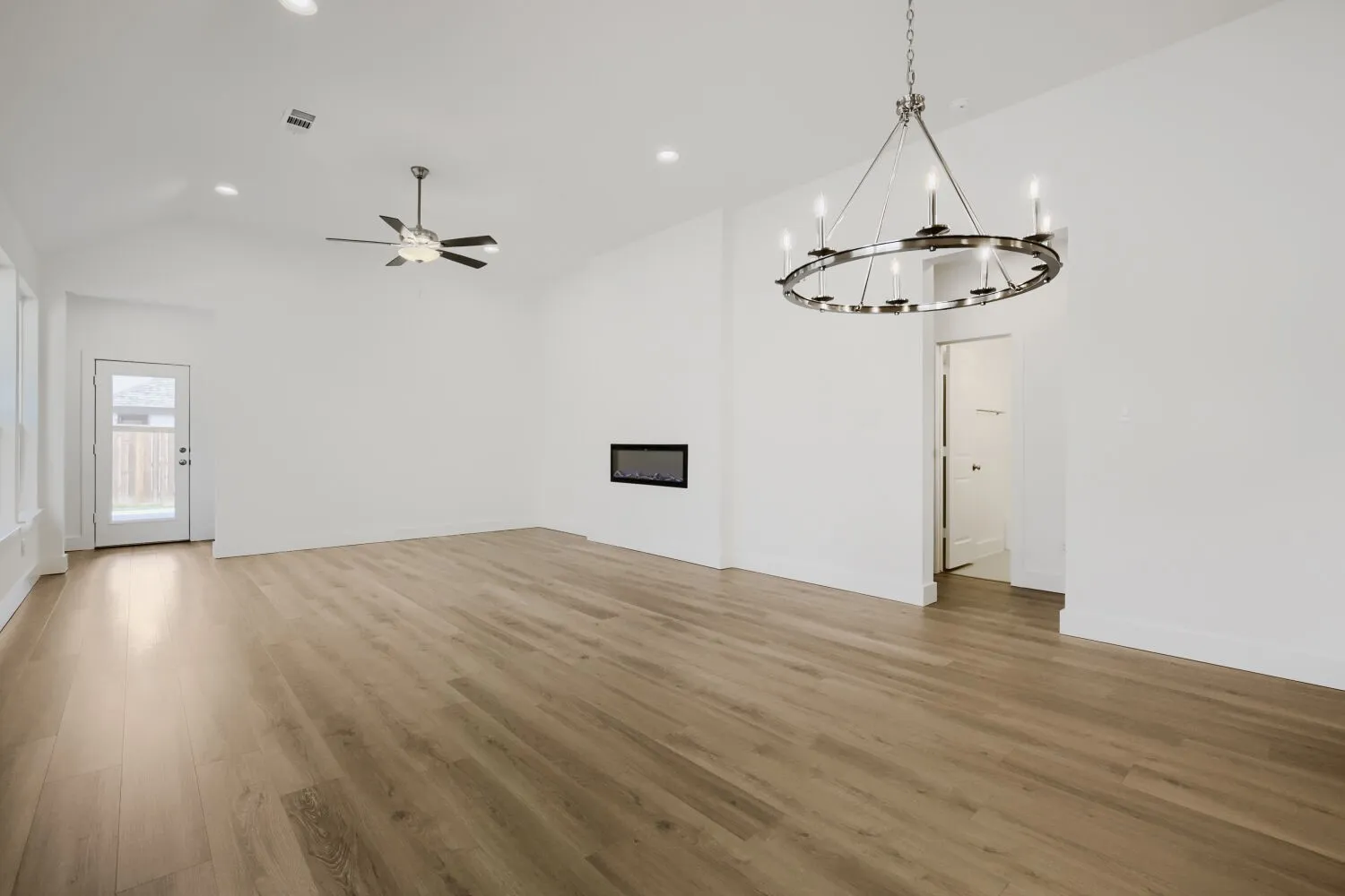 Vaulted ceiling, recessed lighting, wood-finish flooring, linear electric fireplace, and a contemporary chandelier
