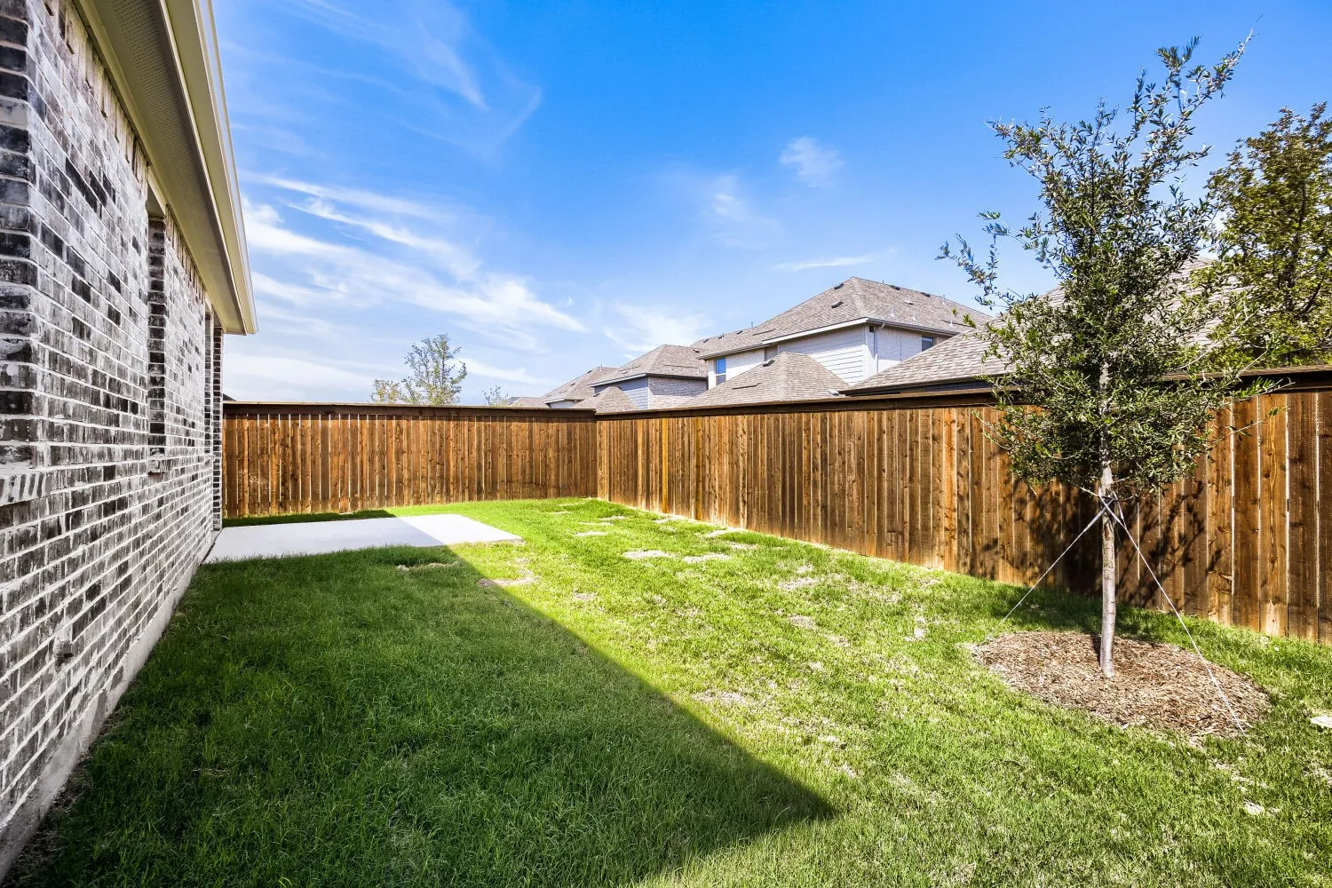 Expansive backyard featuring a brick exterior, privacy fencing, a manicured lawn, and a concrete patio