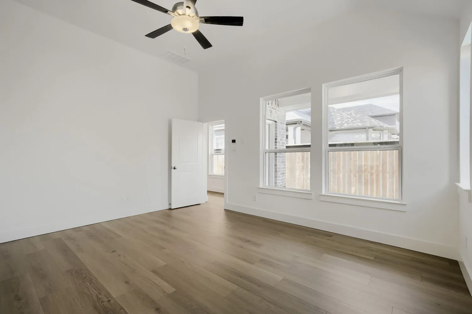 Vaulted ceiling, ceiling fan with integrated lighting, wood-finish flooring, white trim, and multiple windows