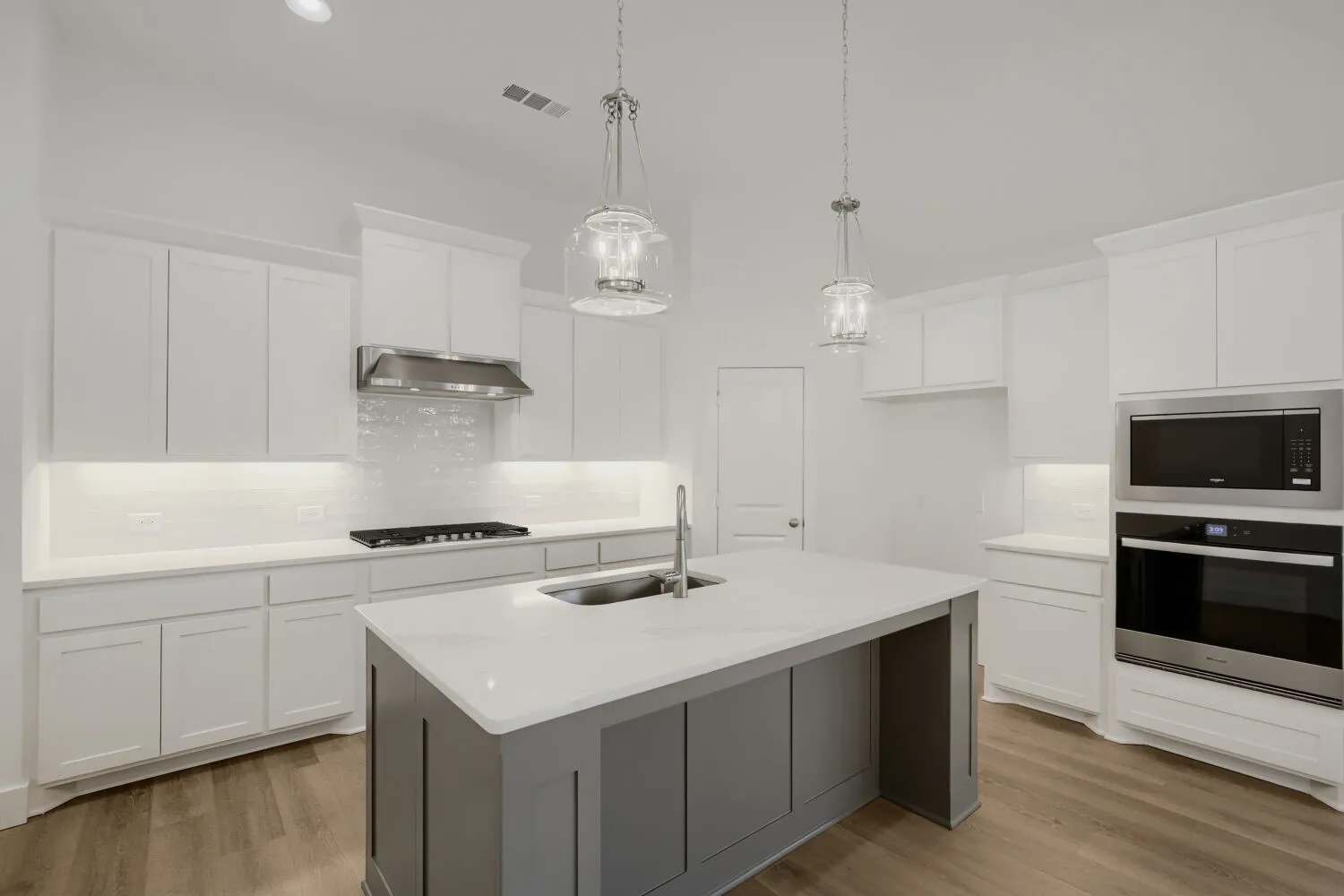 Kitchen with white shaker cabinetry, stainless steel appliances, a center island with sink, pendant lighting, and wood-finish flooring