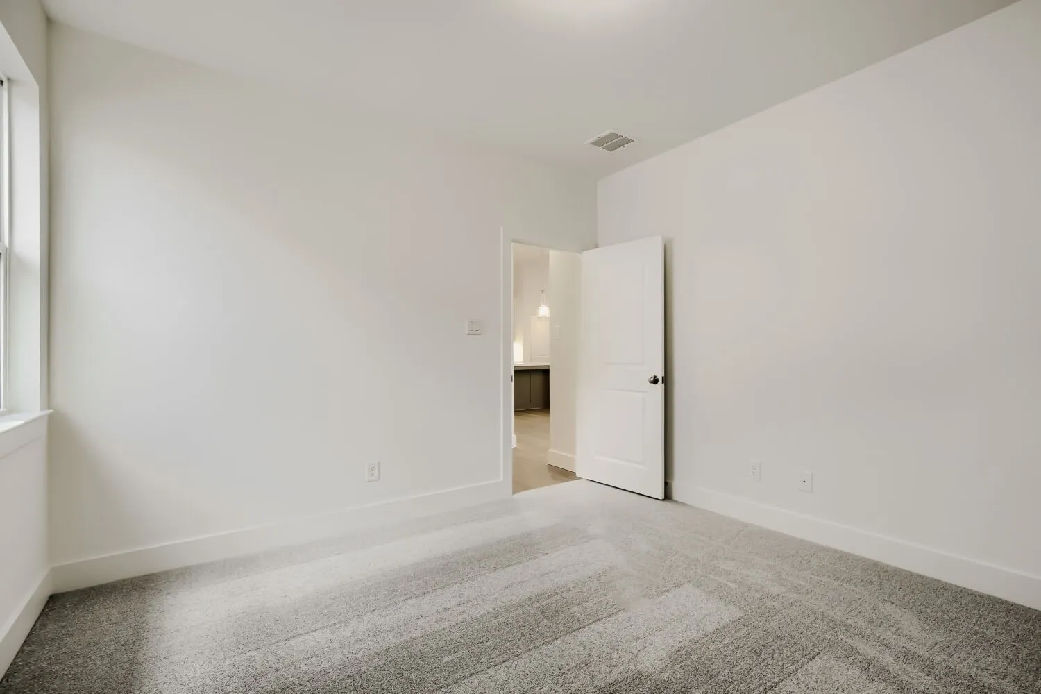 Window with white trim, white walls, light gray patterned carpet, white door with black hardware, and an overhead light fixture