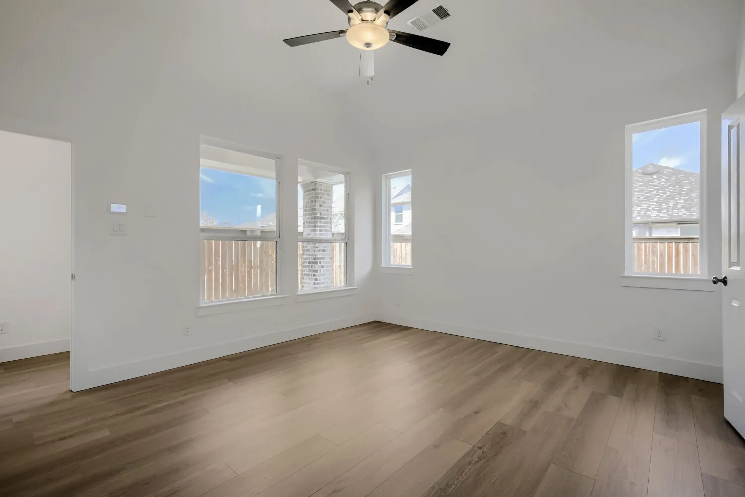 Vaulted ceiling with a ceiling fan, wood-finish flooring, multiple windows, and crisp white walls