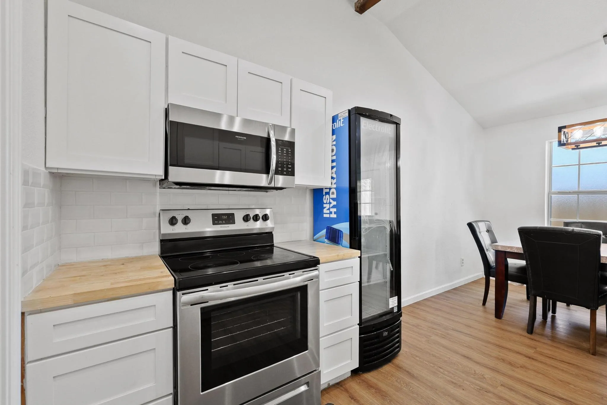 Kitchen area featuring stainless steel appliances, white shaker cabinetry, butcher block countertops, and a subway tile backsplash