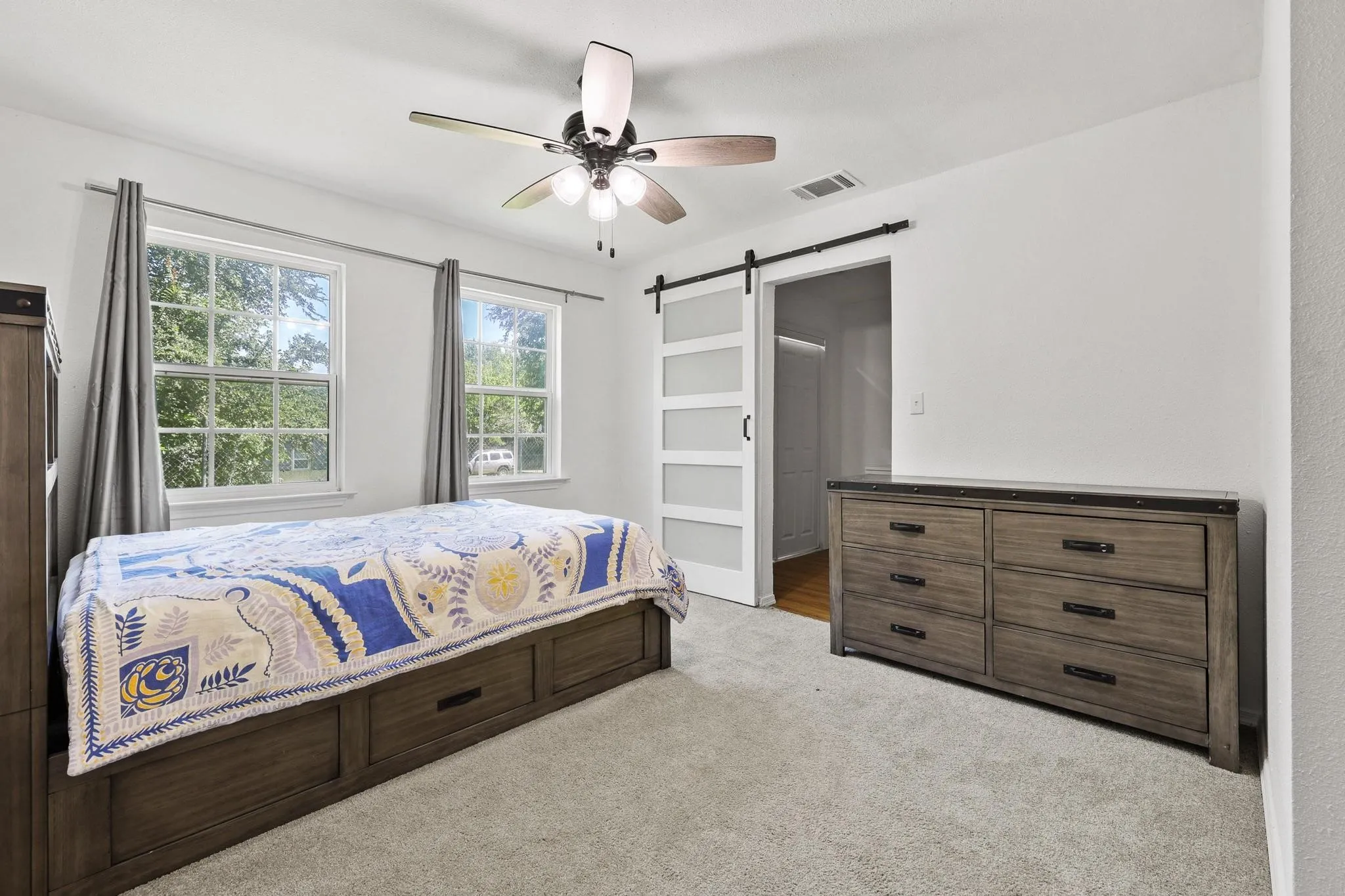 Carpeted room featuring two double-hung windows, a ceiling fan with integrated lighting, and a barn door with frosted glass panels