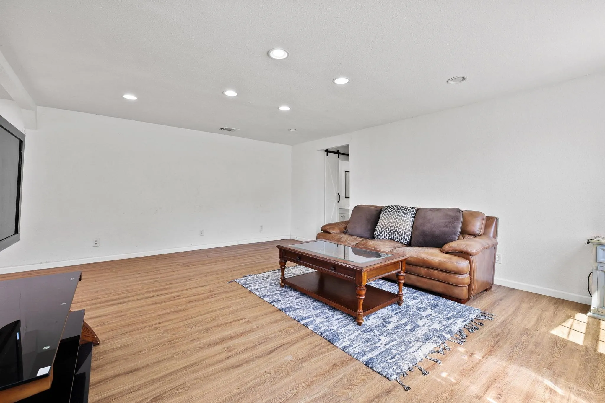 Spacious room featuring wood-finish flooring, recessed lighting, and a white color palette