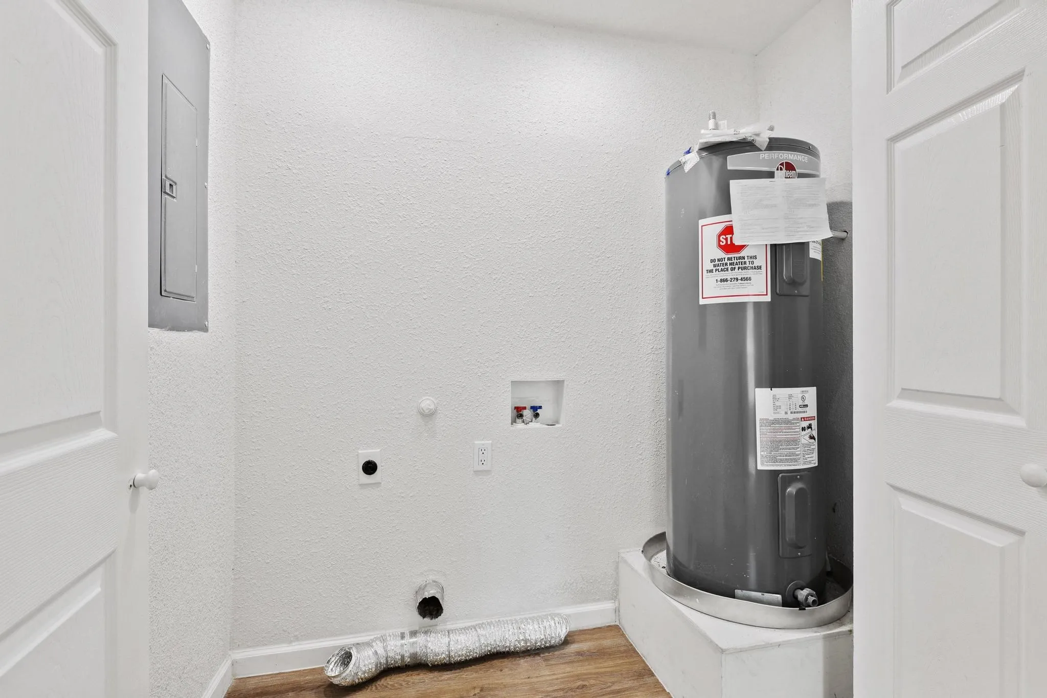 Utility space with a water heater, electrical panel, and wood-finish flooring