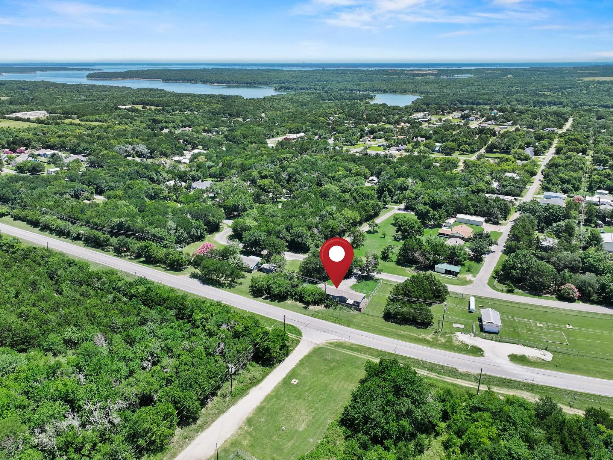 Aerial perspective highlighting a property surrounded by mature trees, featuring a nearby road system and a body of water in the distance