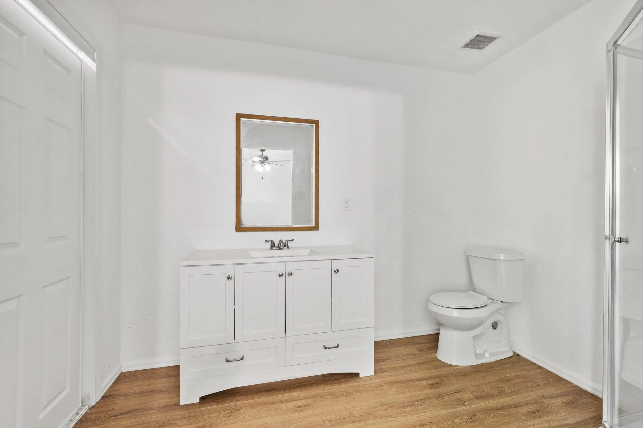 Bathroom featuring wood-finish flooring, a white vanity with integrated sink, a framed mirror, and a glass-enclosed shower