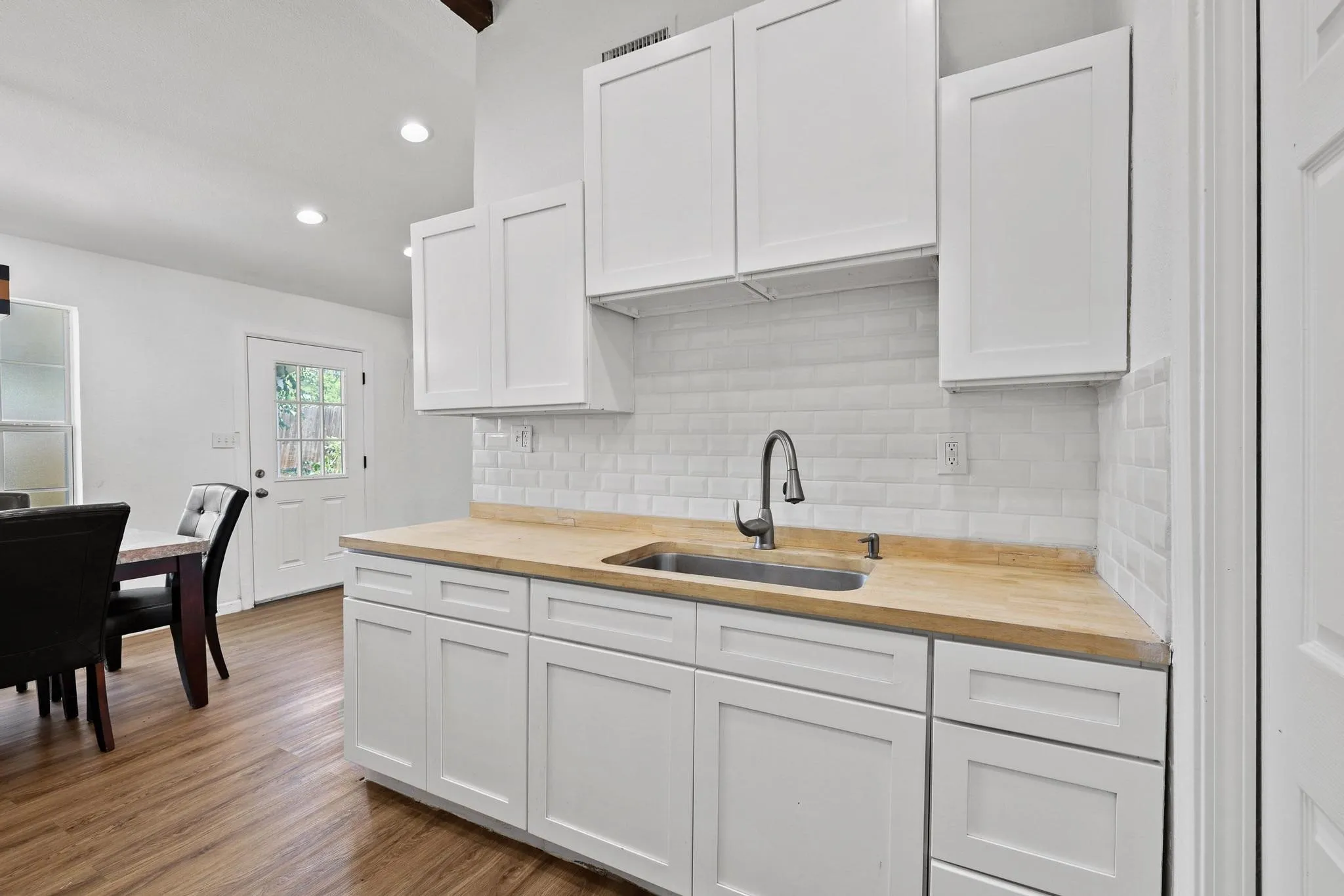 Kitchenette featuring white shaker-style cabinetry, wood-finish countertops, stainless steel sink with a gooseneck faucet, and white subway tile backsplash