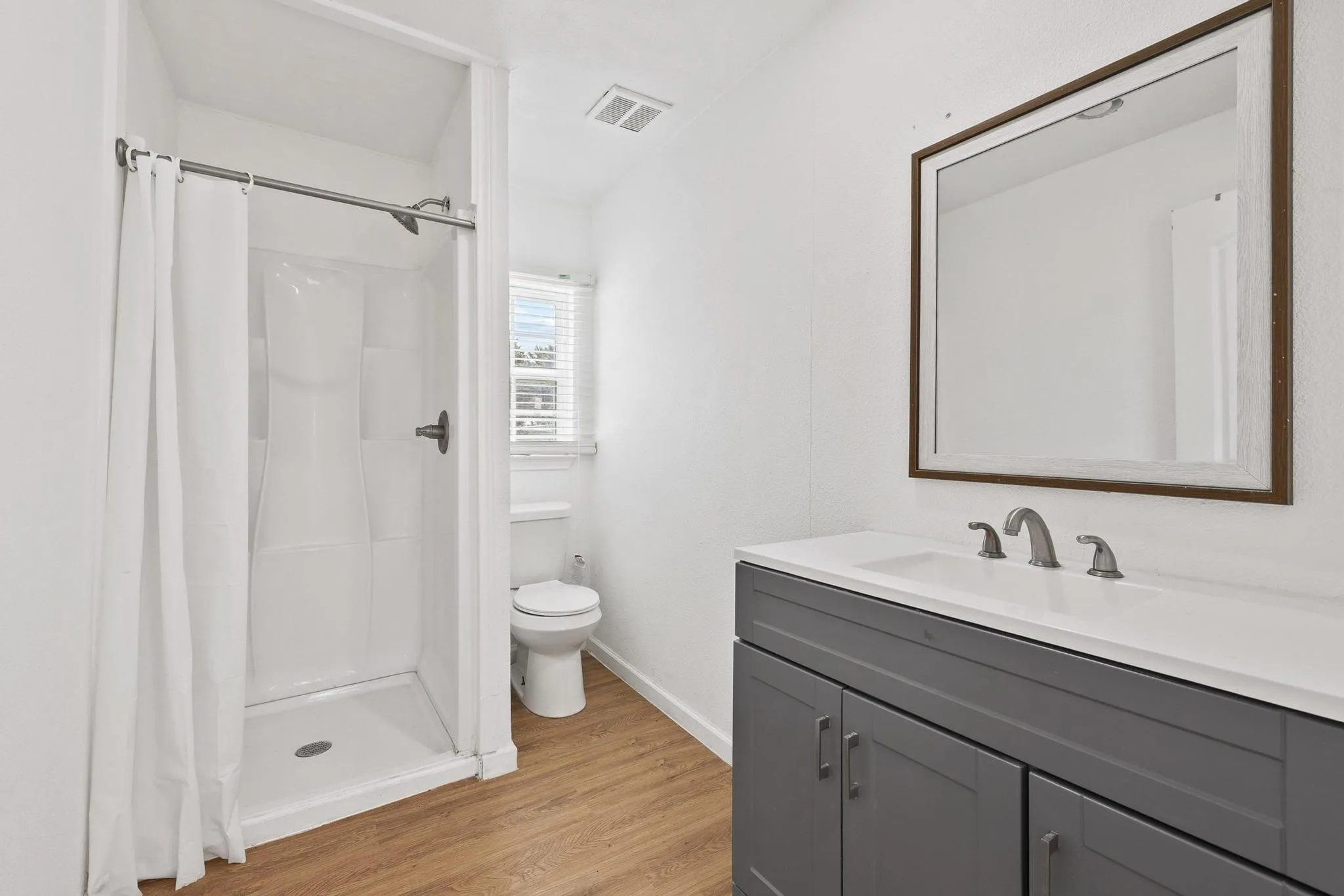 Bathroom featuring a single-piece shower stall, white toilet, and a vanity with a white countertop and gray cabinetry