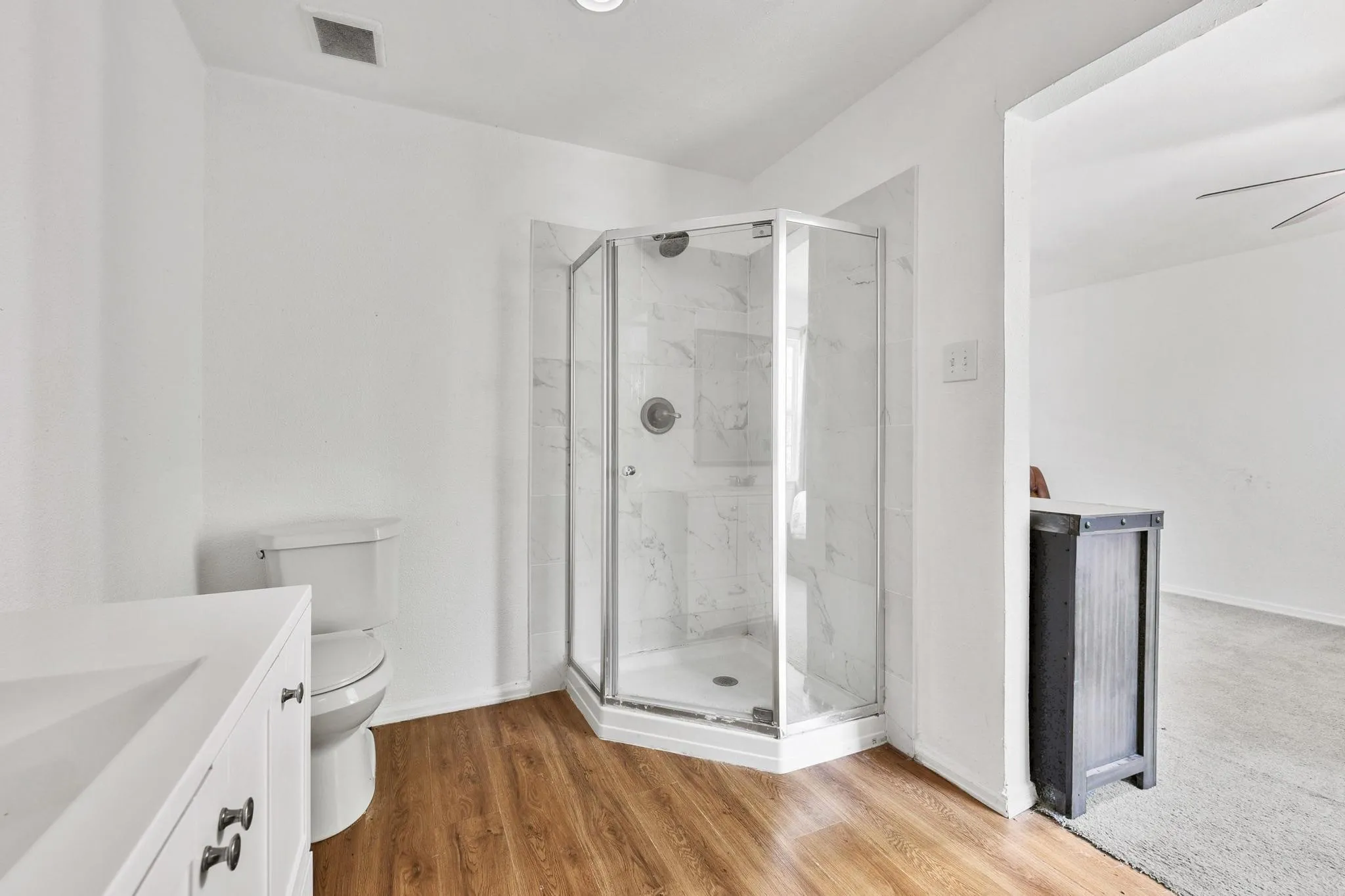 Bathroom featuring a corner shower with glass enclosure and white tiled walls, wood-finish flooring, and a white vanity with an integrated sink