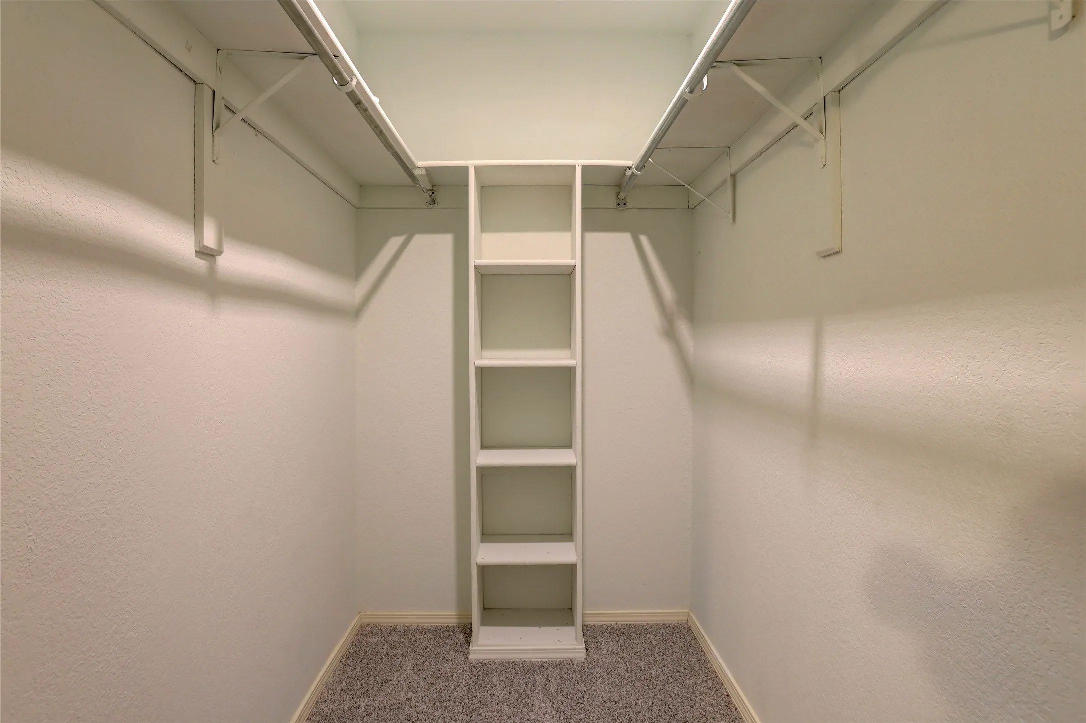 Walk-in closet with built-in shelving, dual hanging rods, and textured carpeting