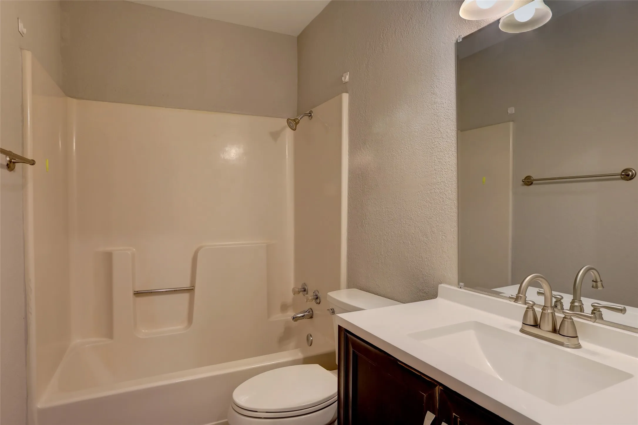 Bathroom featuring a shower-tub combination with grab bar, a vanity with an integrated sink, a large mirror, and a two-light fixture