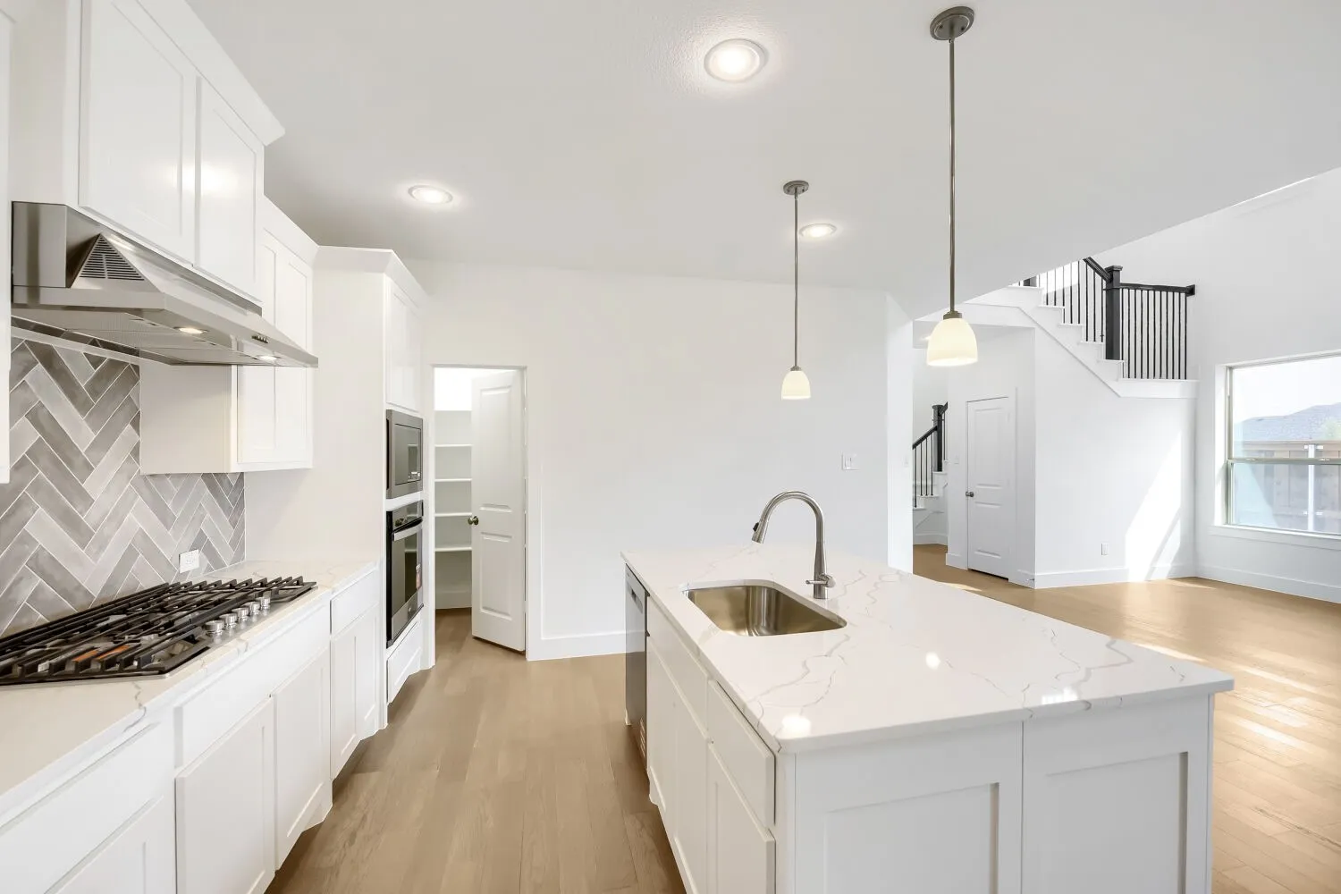 White cabinetry, herringbone tile backsplash, stainless steel appliances, central island with sink, and wood-finish flooring