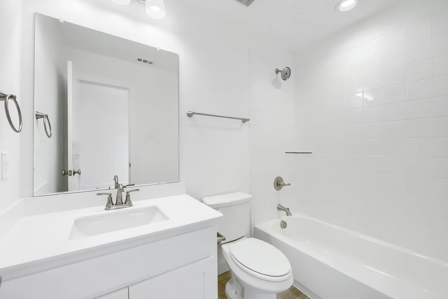 White vanity with integrated sink, brushed nickel faucet, large wall mirror, white tiled shower surround, and a built-in bathtub
