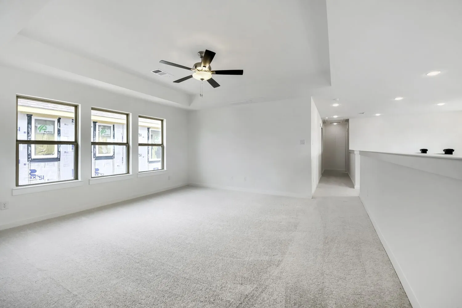 Tray ceiling with a ceiling fan, three windows, light-colored carpeting, recessed lighting, and a white half-wall