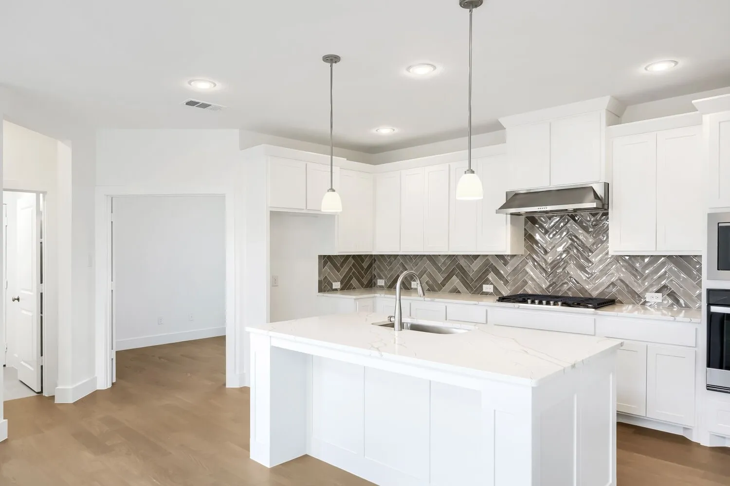 White cabinetry with a herringbone tile backsplash, an island with a sink, stainless steel appliances, and wood-finish flooring