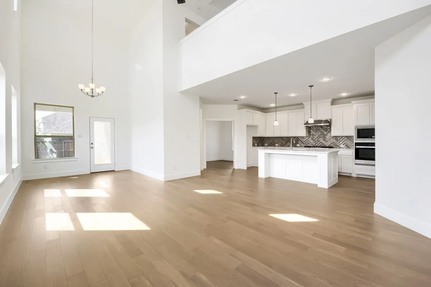 Expansive living area with high ceilings, wood-finish flooring, and a modern chandelier