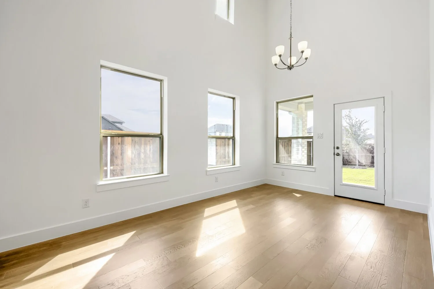 Expansive double-height ceiling, wood-finish flooring, multiple windows, and a glass-paneled exterior door