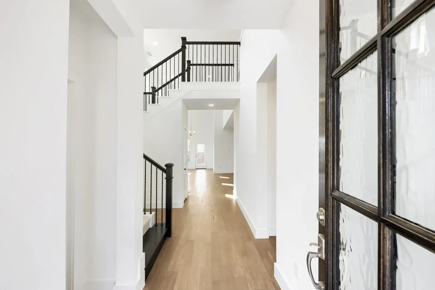 Entryway featuring a decorative glass door, wood-finish flooring, a two-story staircase with black metal balusters, and white walls