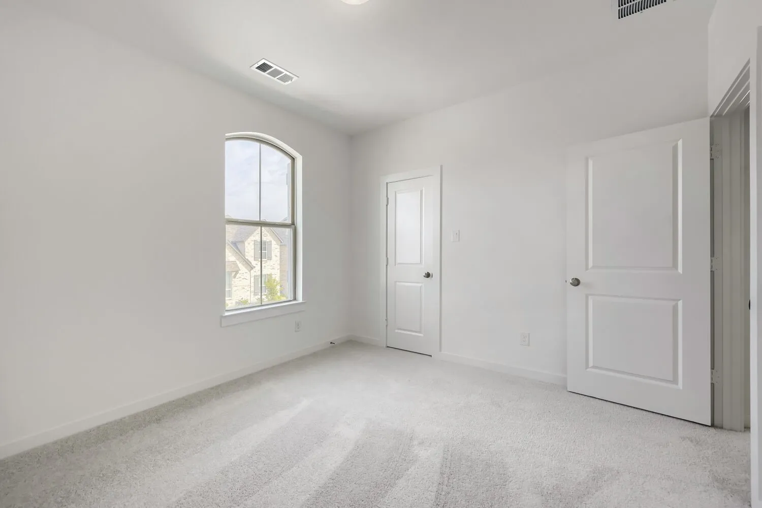 Arched window, white walls, light gray carpet, recessed ceiling light, two panel doors with satin nickel hardware