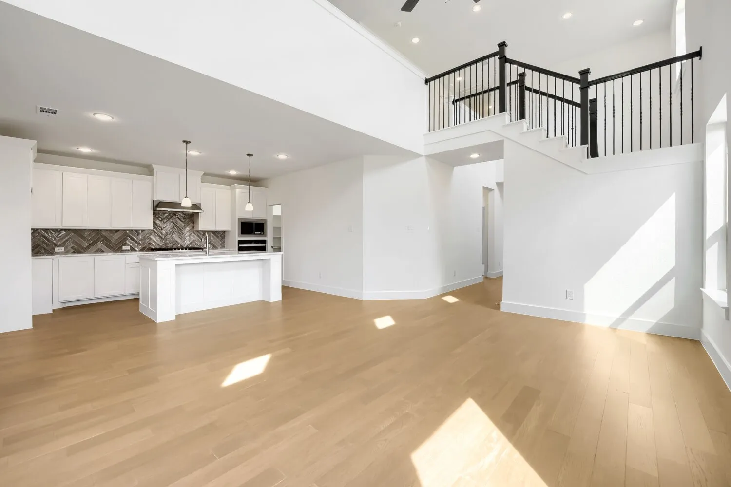 Open-concept living area with high ceilings, wood-finish flooring, a kitchen island, and a staircase with black iron balusters