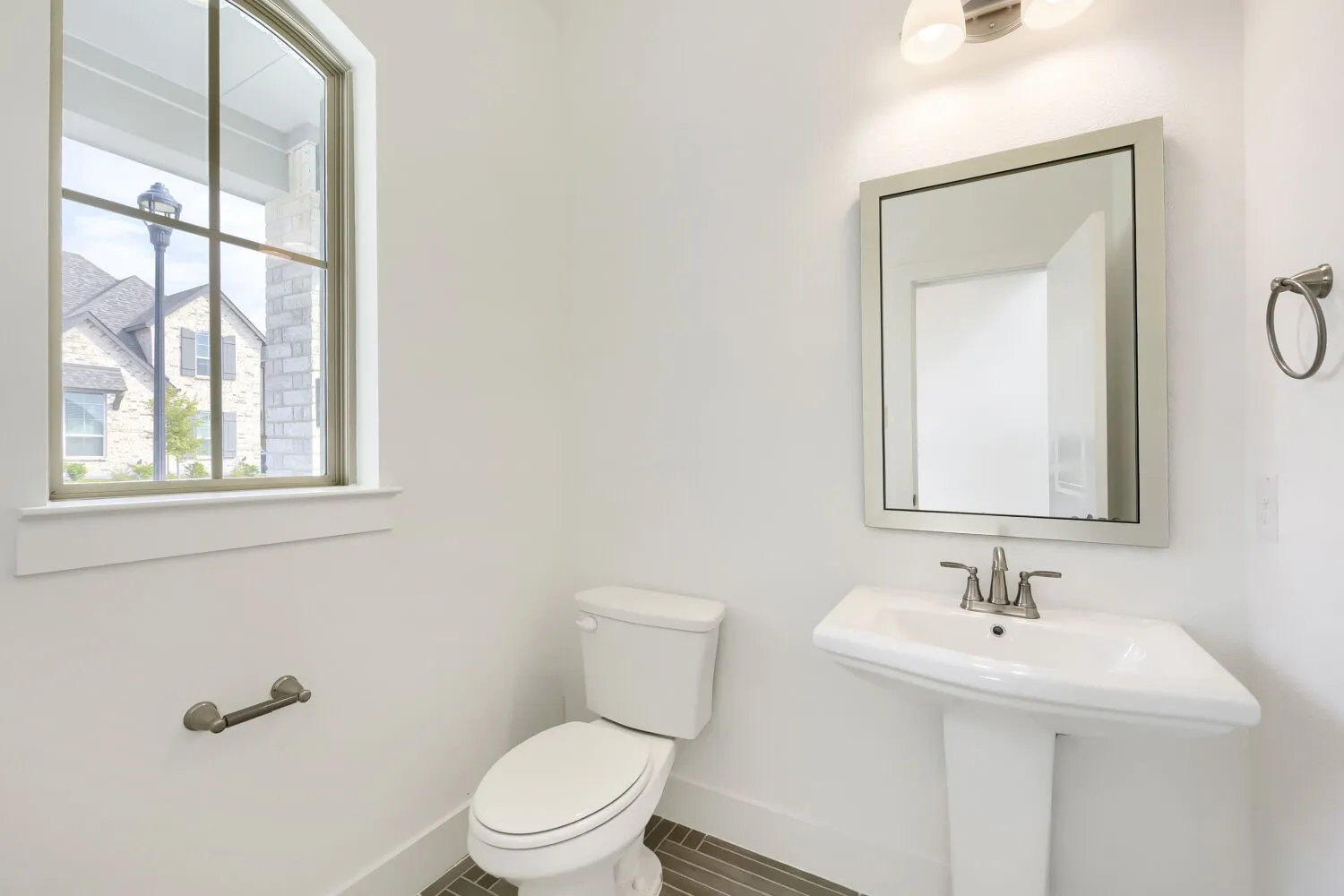 Pedestal sink with a polished chrome faucet, rectangular framed mirror, and an arched window