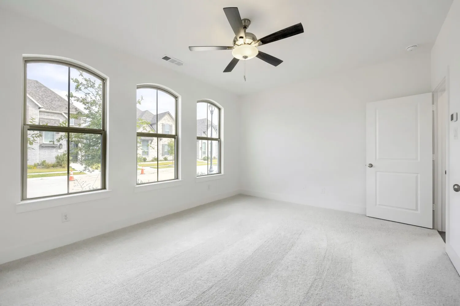 White walls with light-toned carpet flooring, three arched windows, and a ceiling fan with integrated lighting