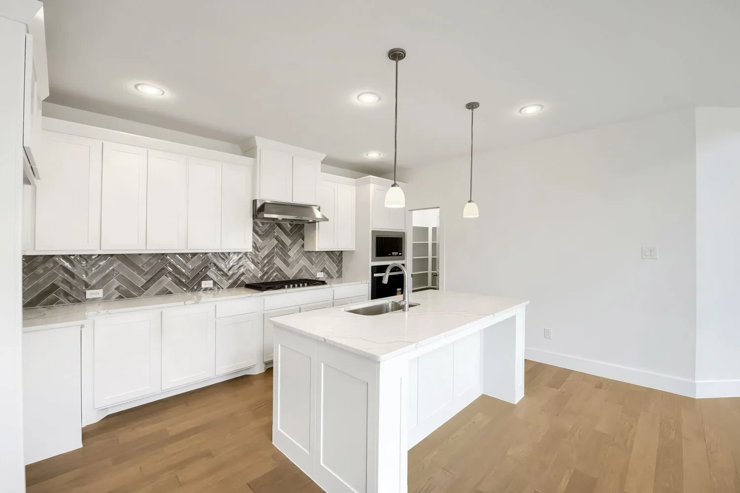 White cabinetry, herringbone tile backsplash, white countertop, stainless steel appliances, and wood-finish flooring