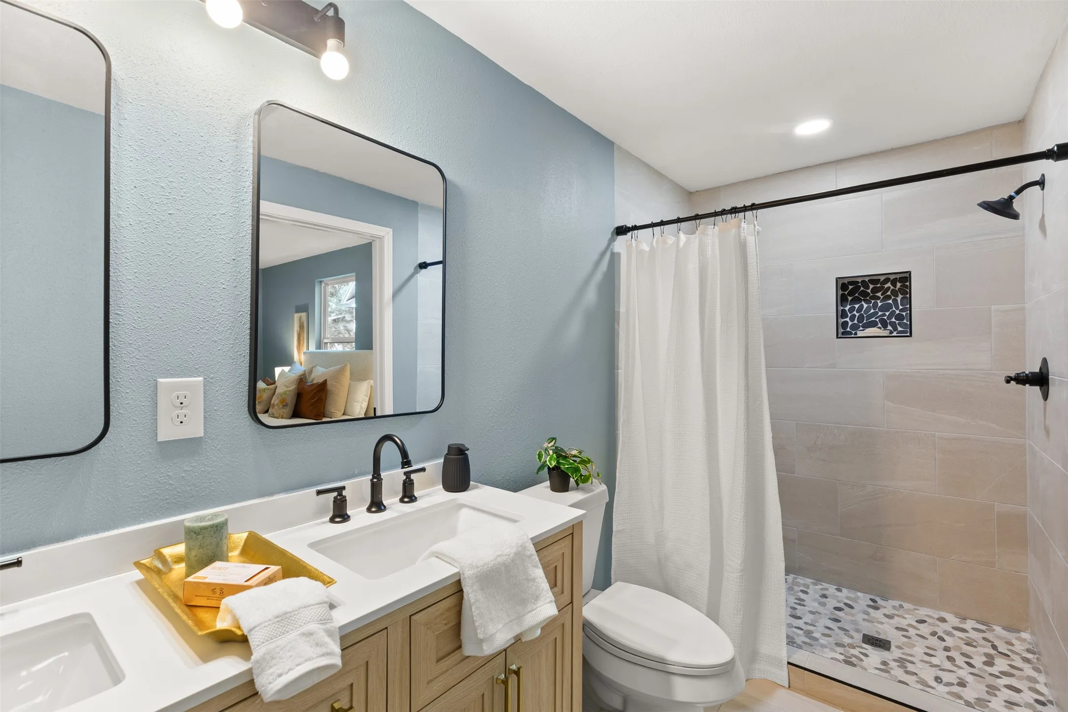 Modern bathroom featuring a dual vanity with light wood cabinetry, white countertops, and matte black fixtures
