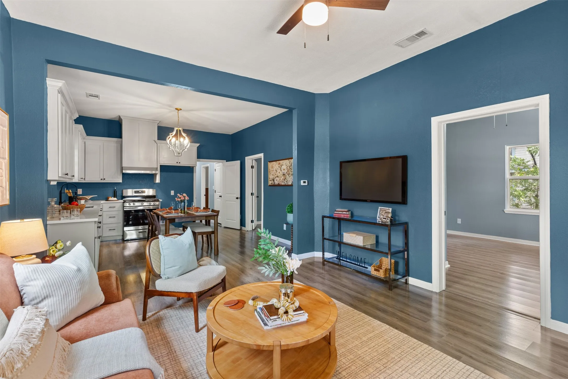 Open-concept living space featuring wood-finish flooring, a contemporary ceiling fan, and a kitchen with white cabinetry, stainless steel appliances, and a built-in range hood