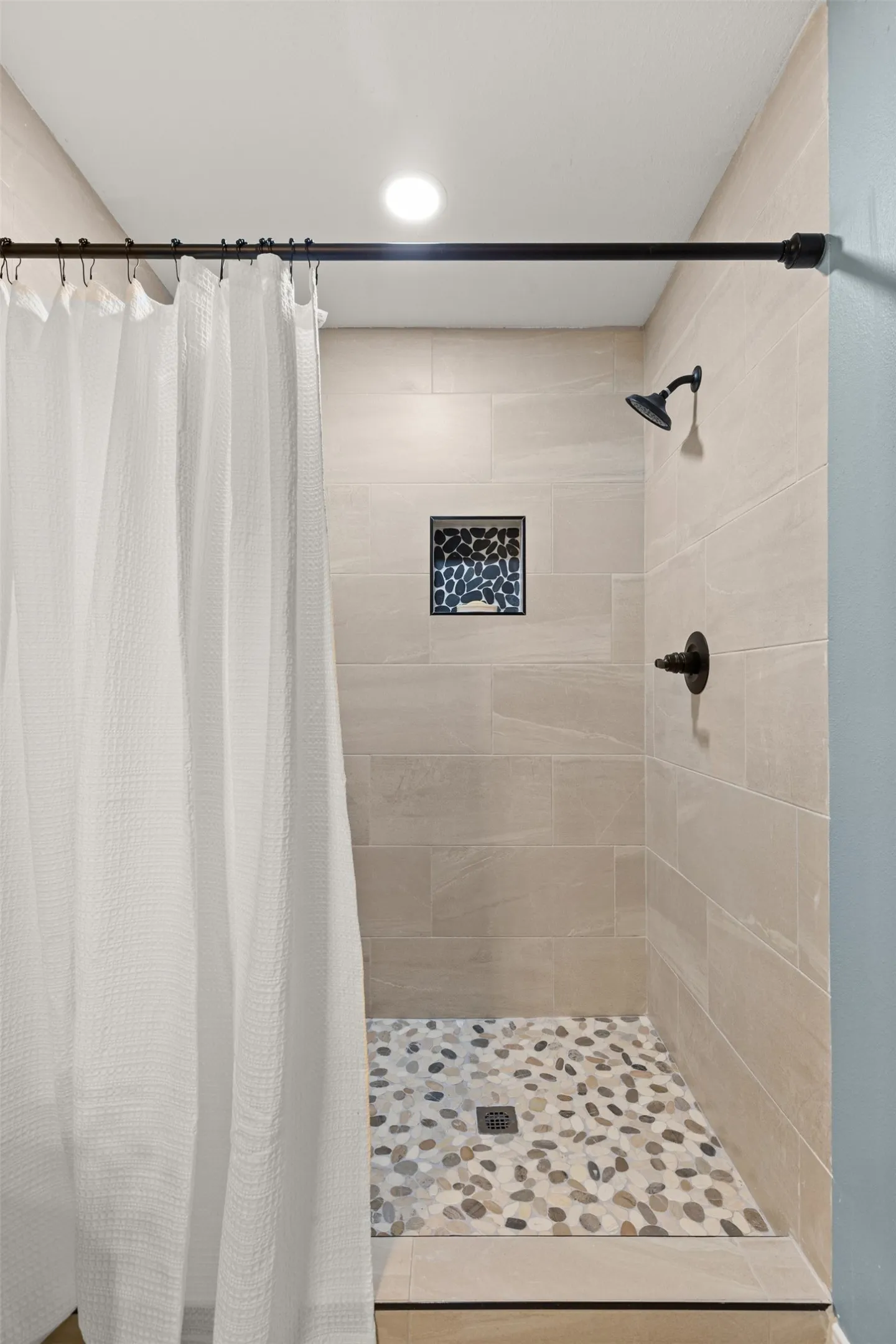Shower enclosure with large format tiled walls, a pebble-finish shower floor, and a recessed niche with mosaic tile accents