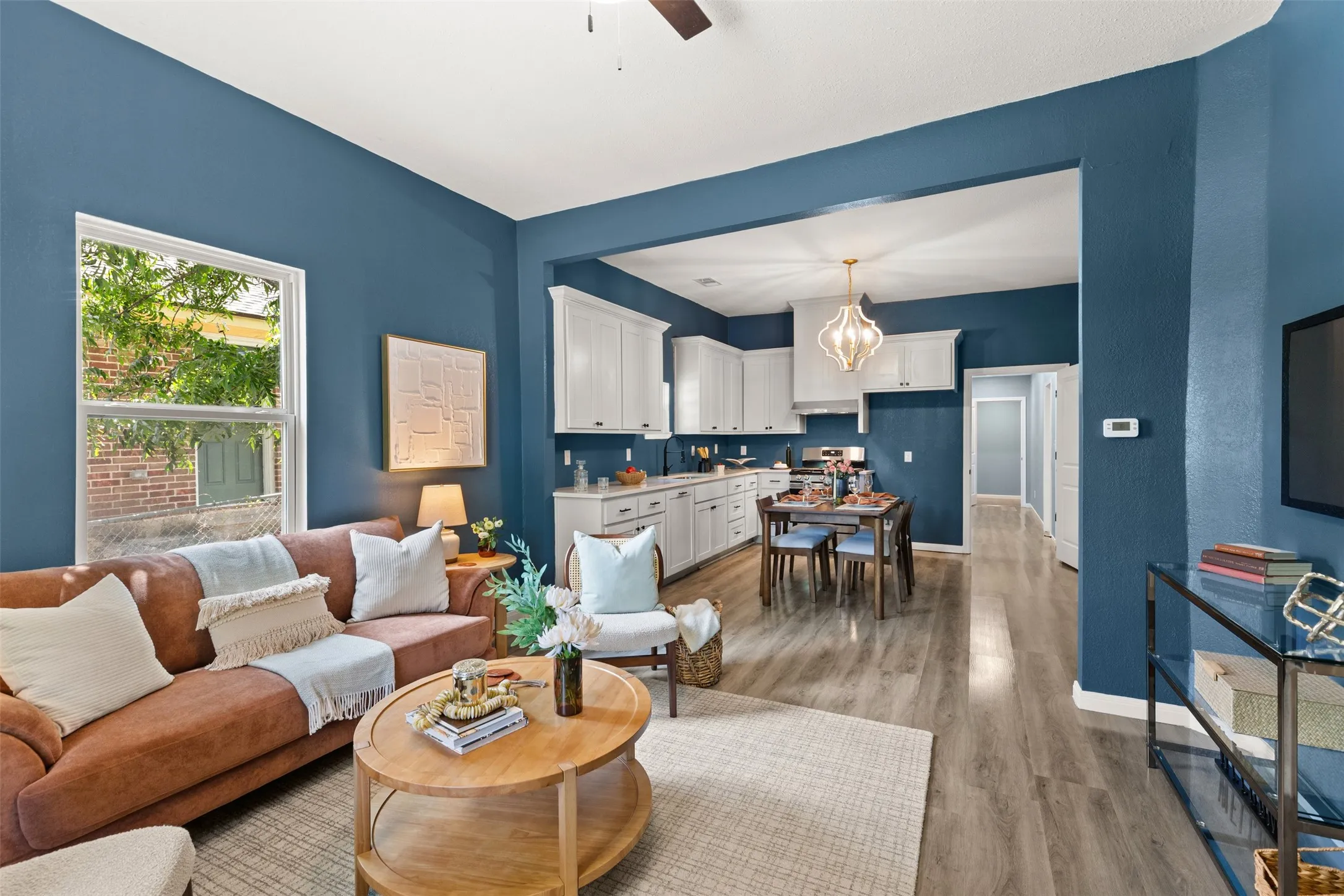 Open-concept living space featuring wood-finish flooring, white cabinetry, a built-in kitchen range hood, and a decorative chandelier