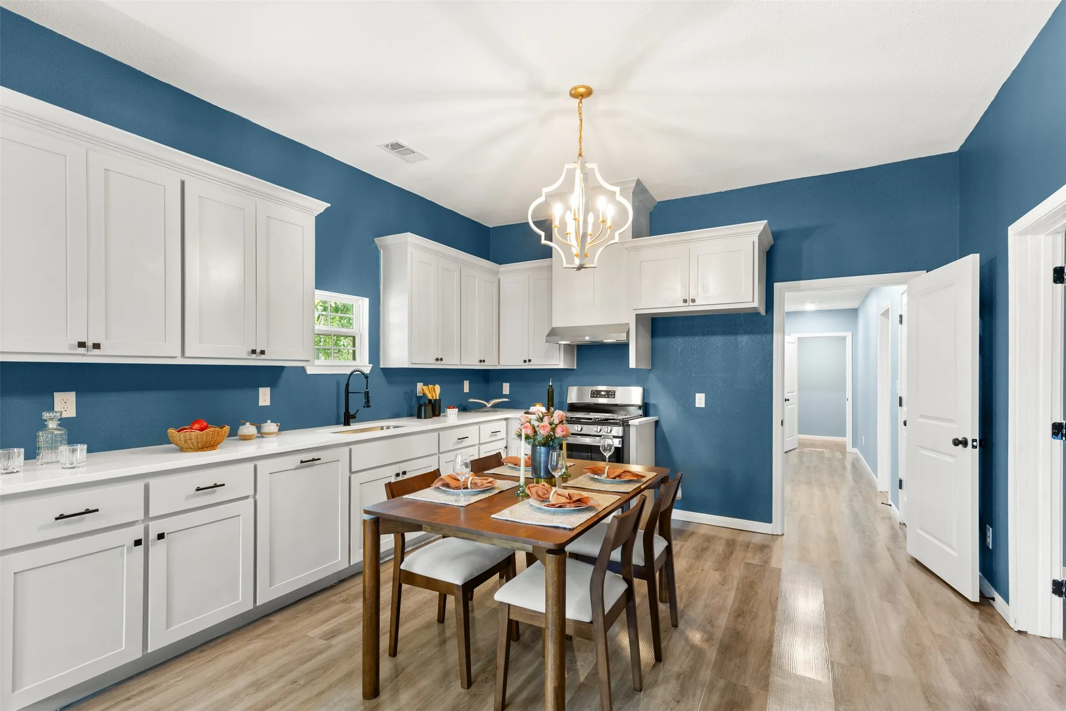 Kitchen featuring white shaker-style cabinetry, light-toned countertops, stainless steel appliances, wood-finish flooring, and a decorative overhead light fixture