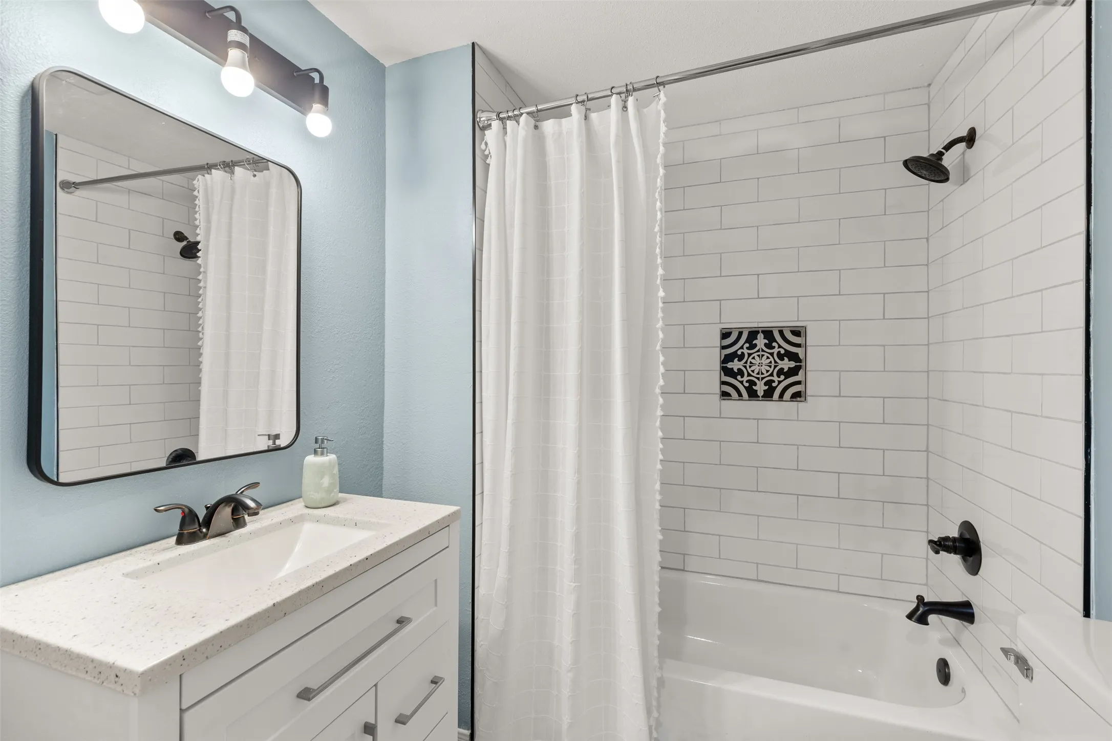 Bathroom featuring a white subway tile shower surround with decorative accent tile, a white vanity with a light-colored countertop, and contemporary black fixtures