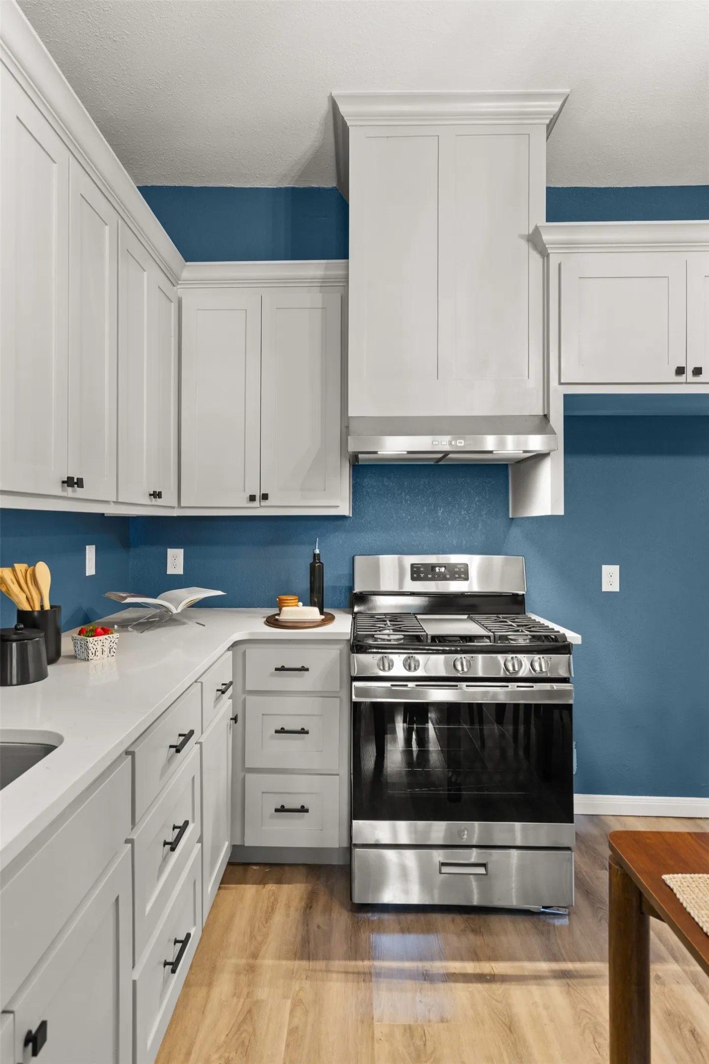 Contemporary kitchen featuring white shaker cabinetry, stainless steel range and hood, white countertops, and wood-finish flooring