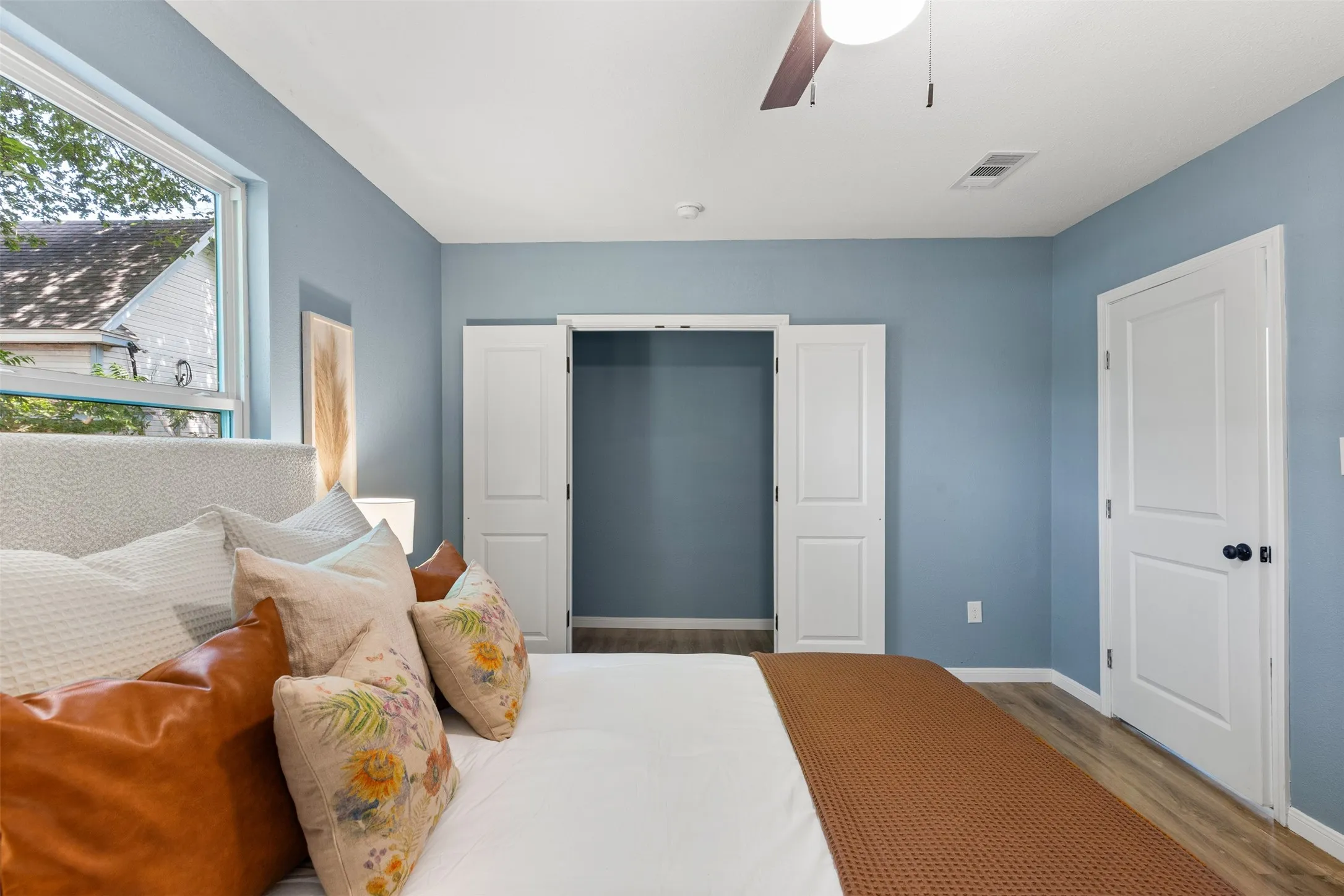 Interior room featuring light blue walls, wood-finish flooring, a contemporary ceiling fan, and white paneled doors