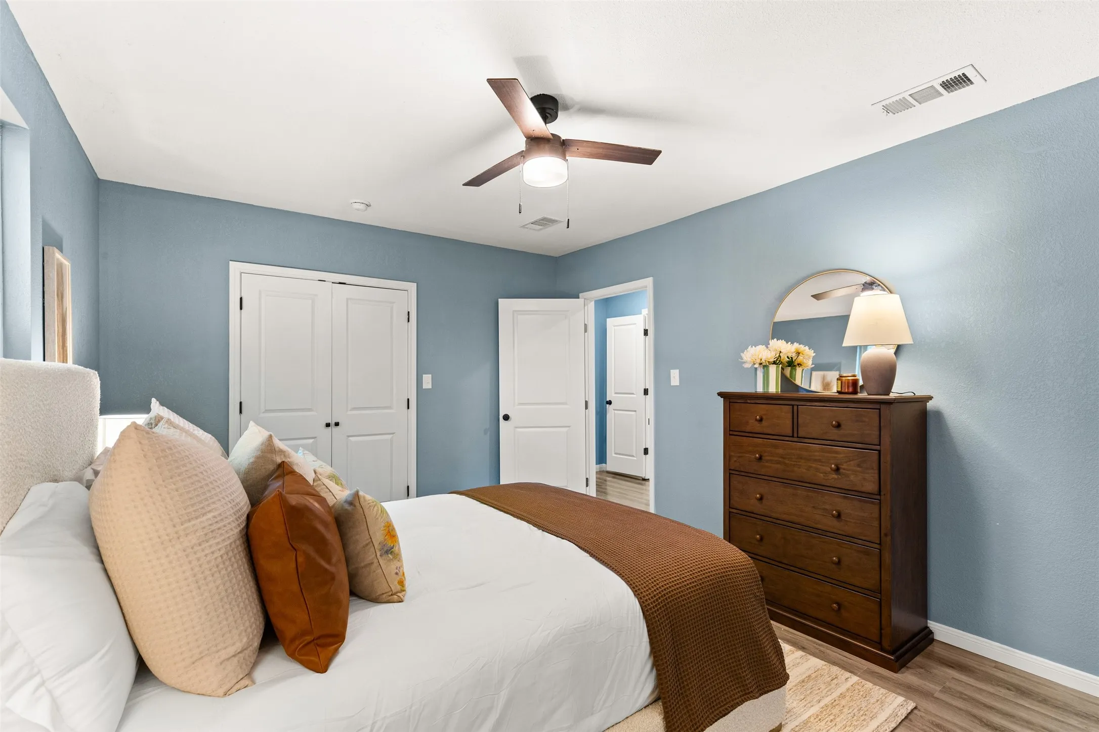 Bedroom featuring light blue walls, wood-finish flooring, a ceiling fan with integrated lighting, and white bi-fold closet doors