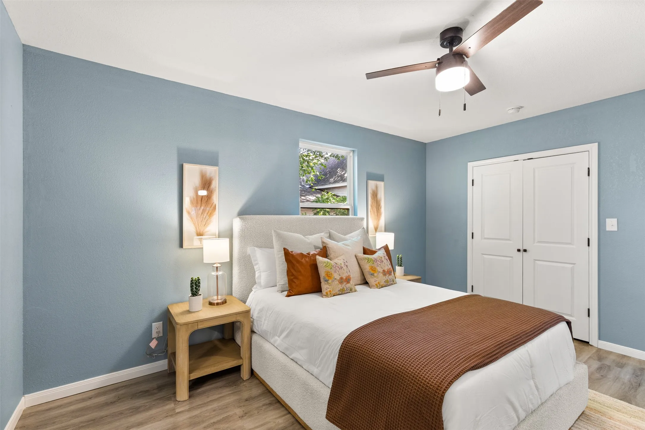 Bedroom featuring light blue walls, wood-finish flooring, a contemporary ceiling fan with light, and white bi-fold closet doors